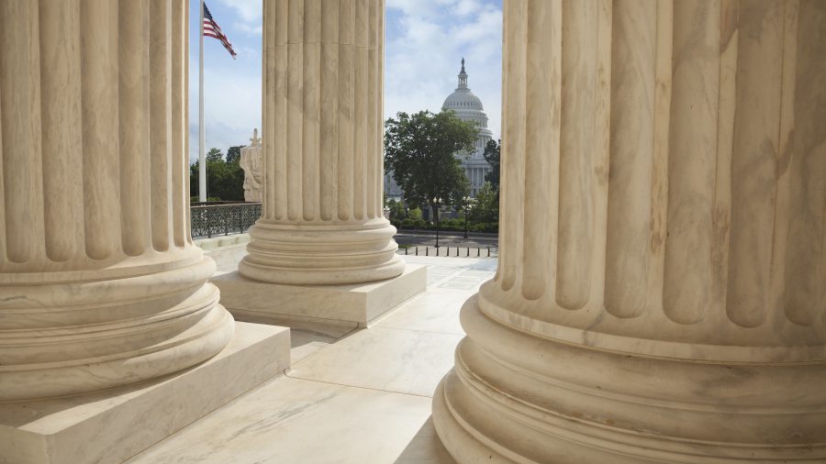 Close up of the columns  of the Supreme Court building with an American flag and the US Capitol in the background